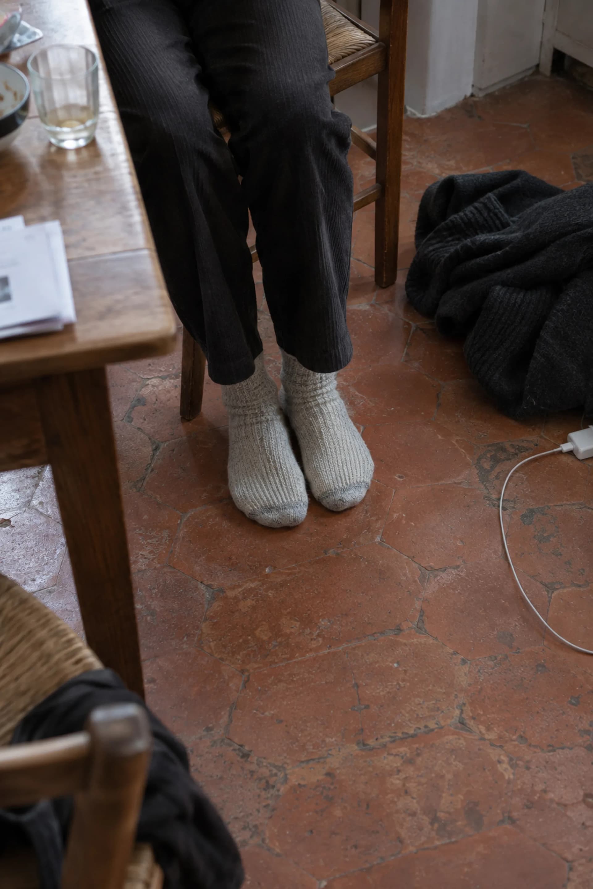 Des pieds en chaussettes posés à plat sur un parquet clair, près d'un plaid corail.